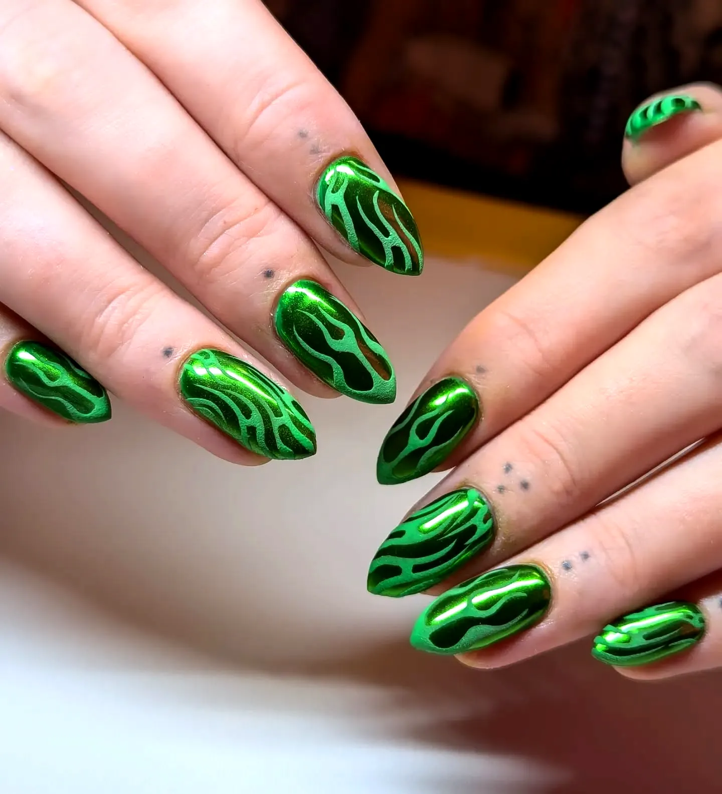 Bold elongated almond tribal nails with vibrant metallic green and intricate flame patterns