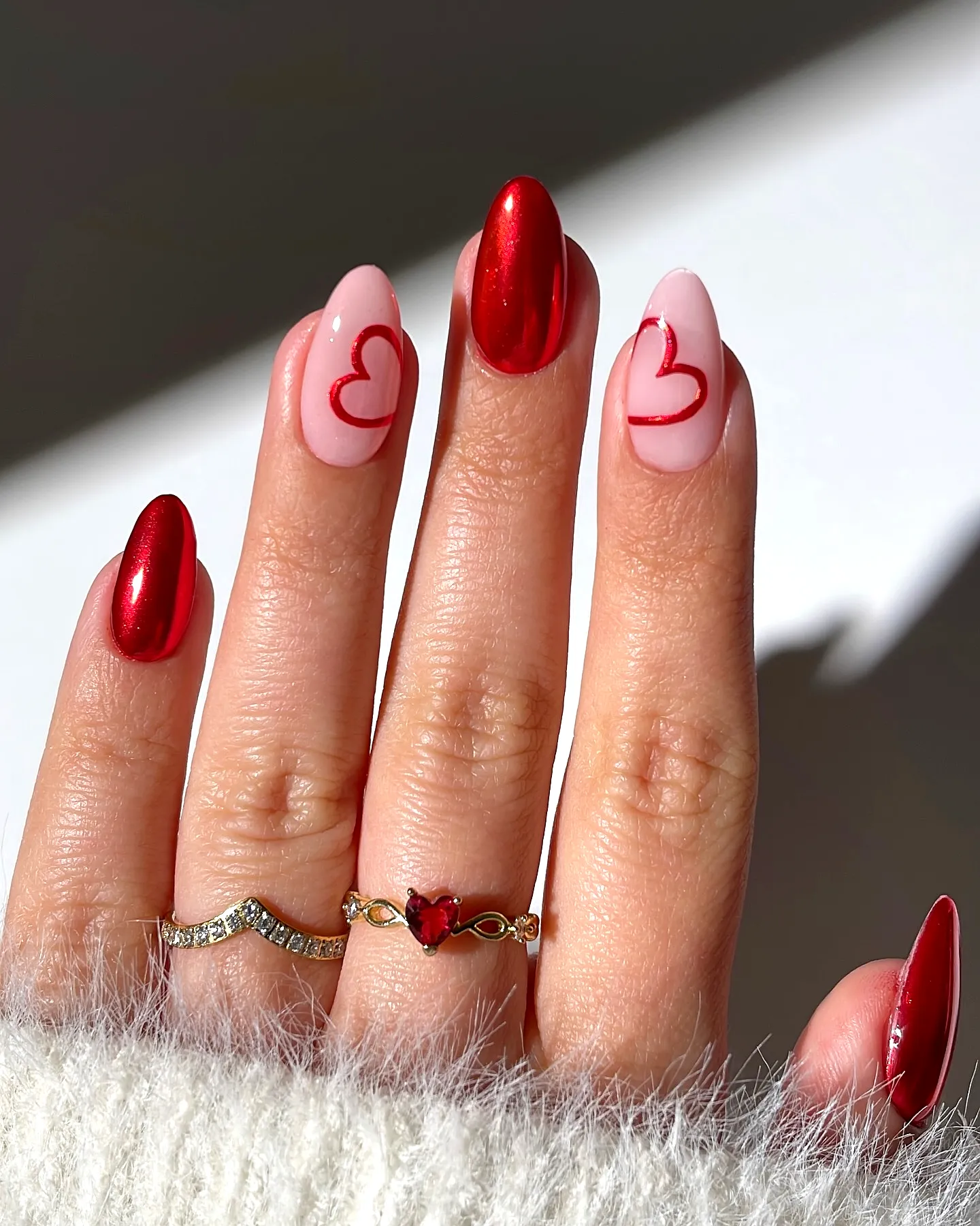Charming oval and almond shaped red nails with heart outlines and metallic accents