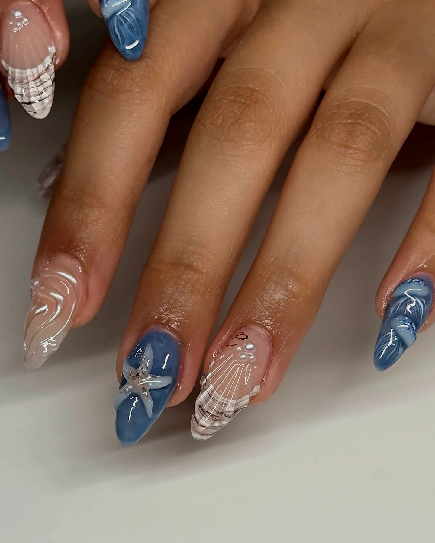 Chic Almond-Shaped Beach Nails in Blue with White Marble Patterns and Seashell Motifs