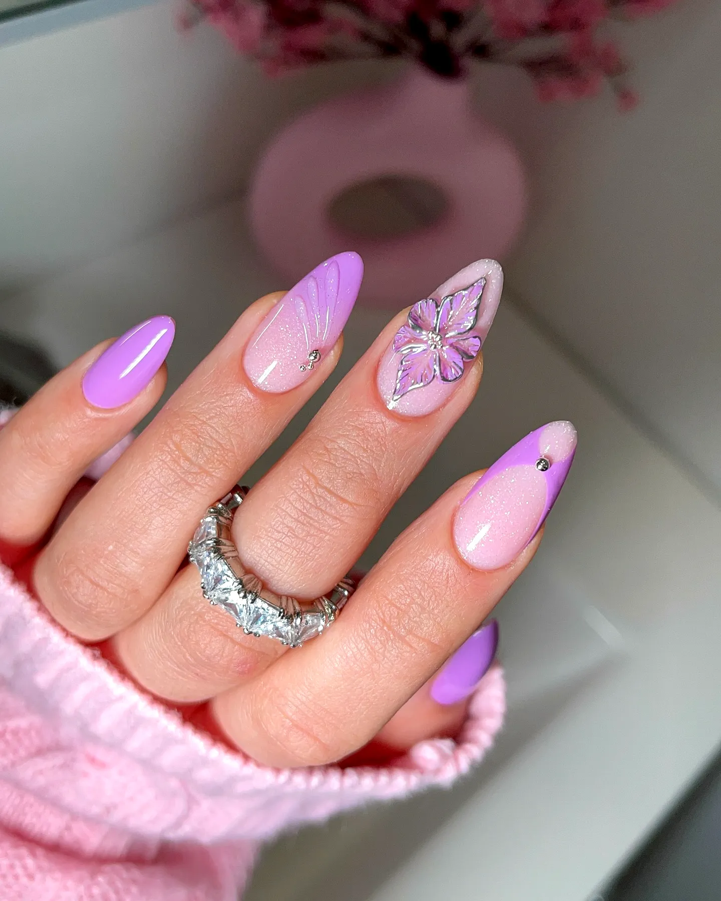 Chic pastel purple spring nails with flower accents and shimmering gems on stiletto shape