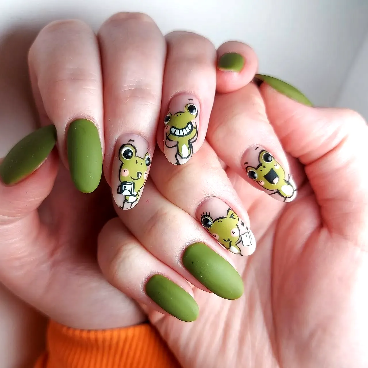 Cute almond olive green nails with whimsical frog illustrations and playful designs