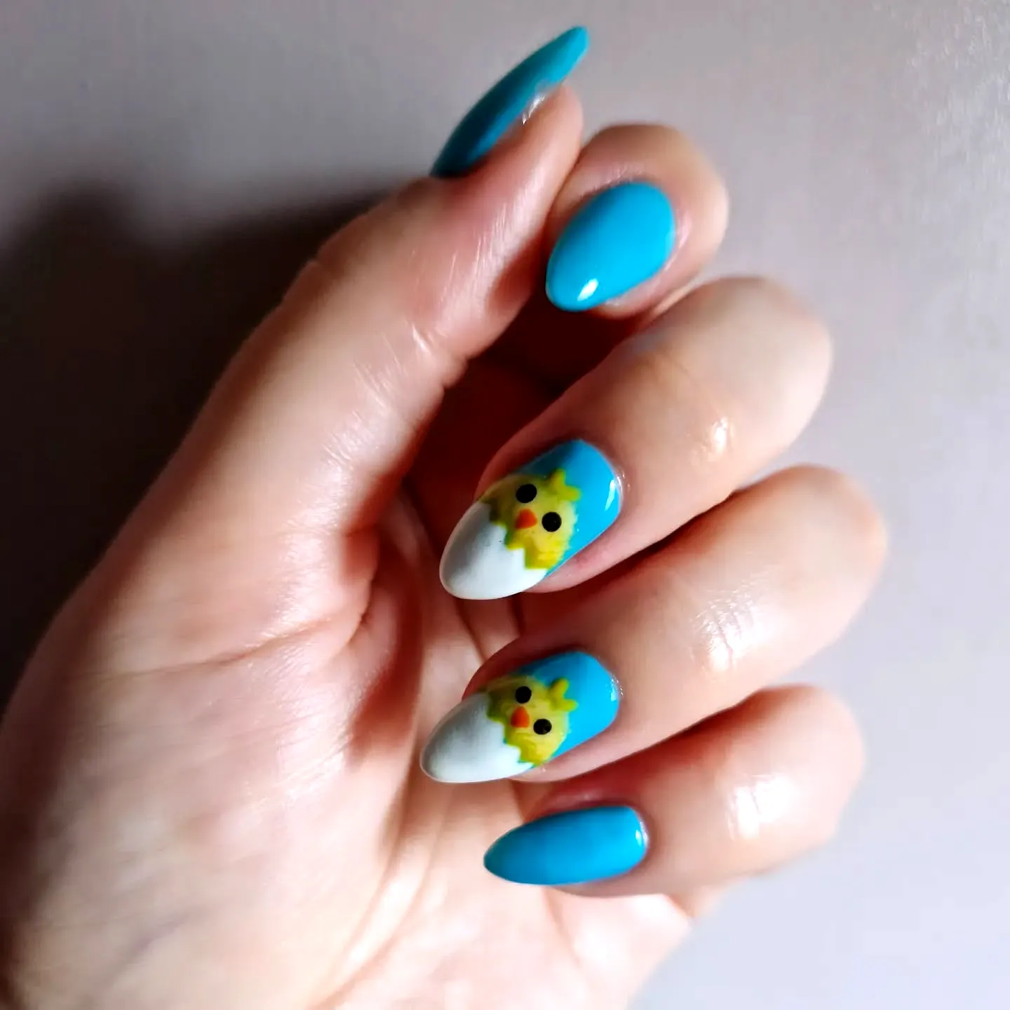 Cute almond-shaped Easter nail designs with bright turquoise and white colors featuring a playful egg-inspired yellow chick