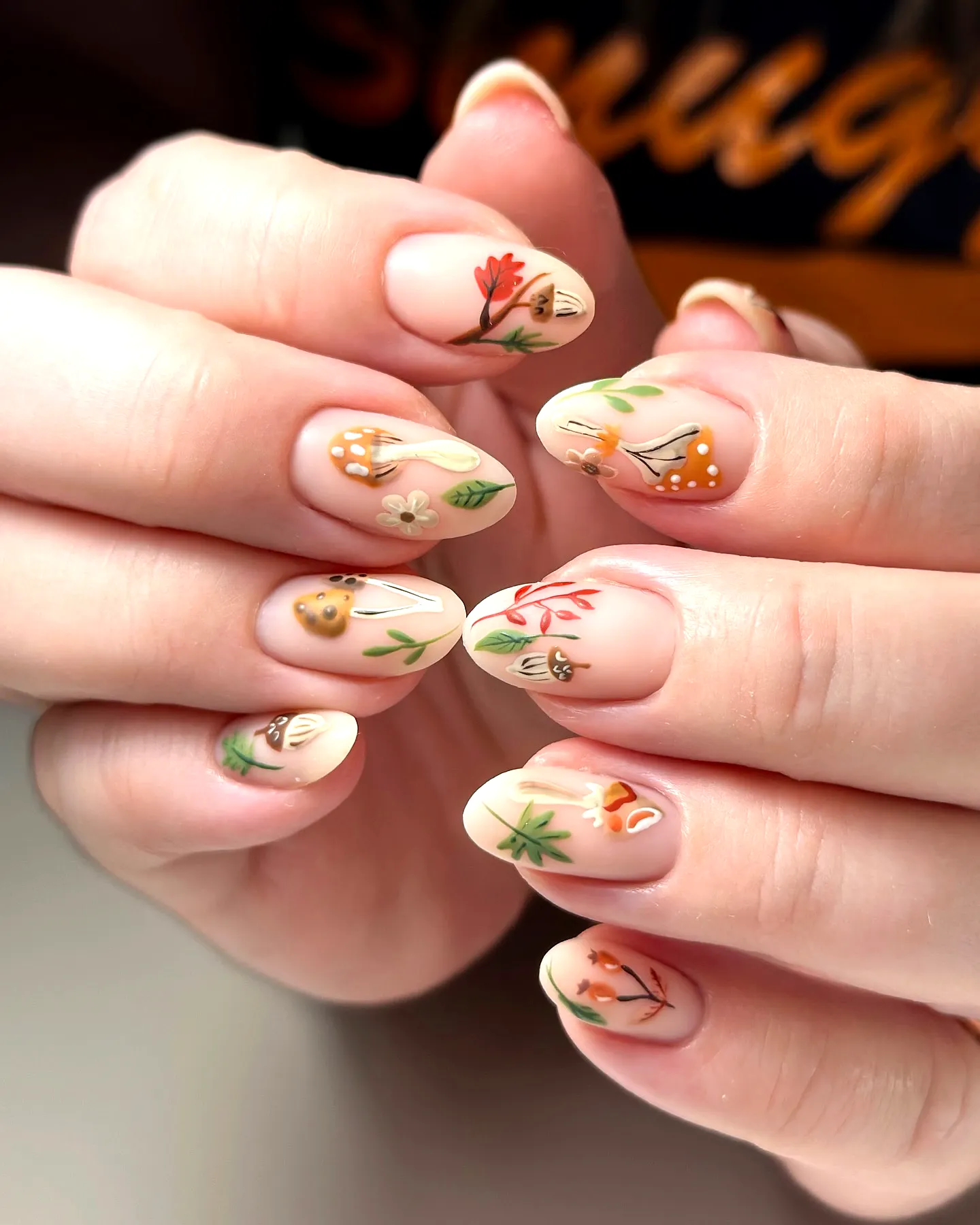 Cute almond-shaped fall nail designs with a neutral base and delicate floral illustrations in soft shades of green orange and yellow