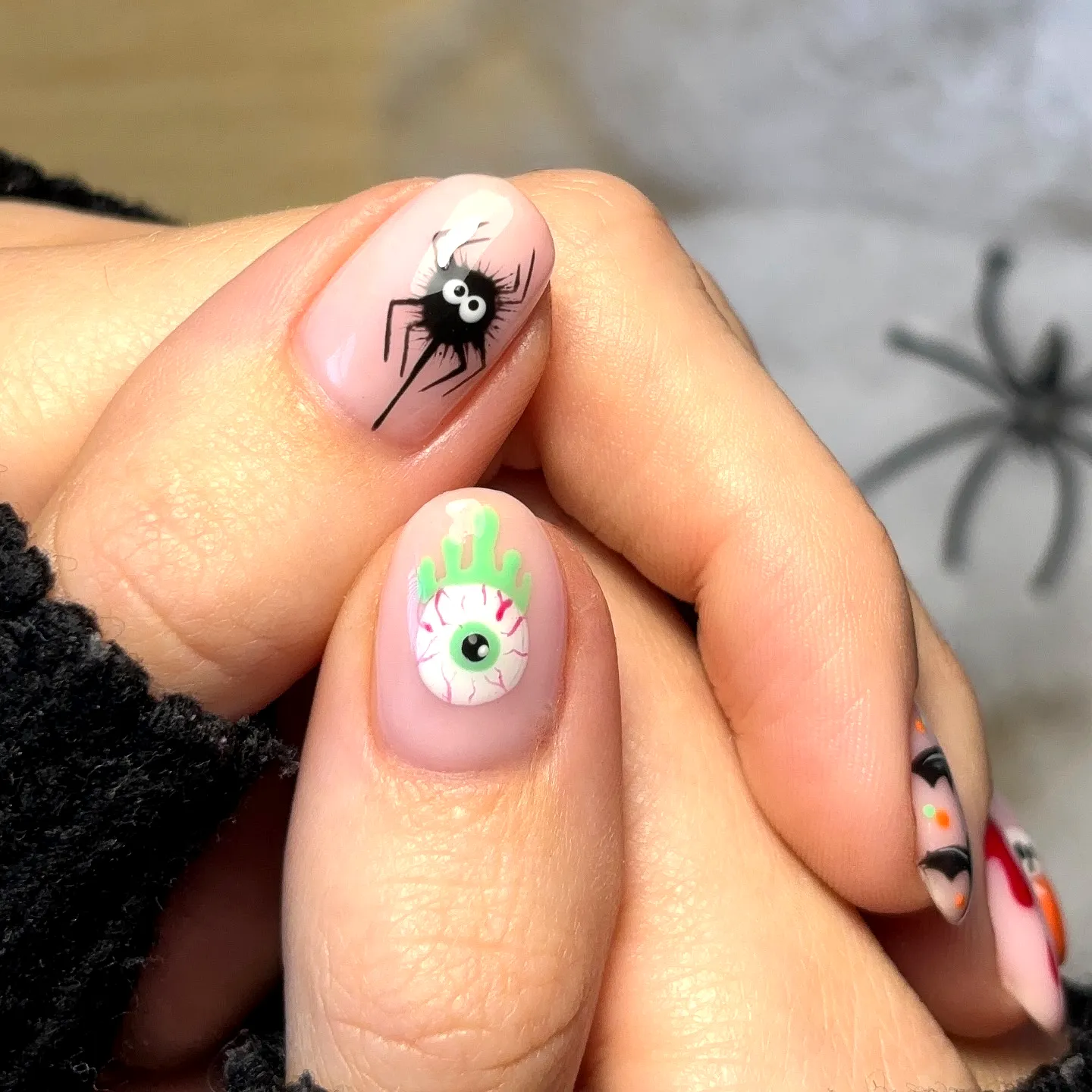 Cute Almond Shaped Halloween Nails with Black Spider and Cartoonish Eye on Soft Nude Background