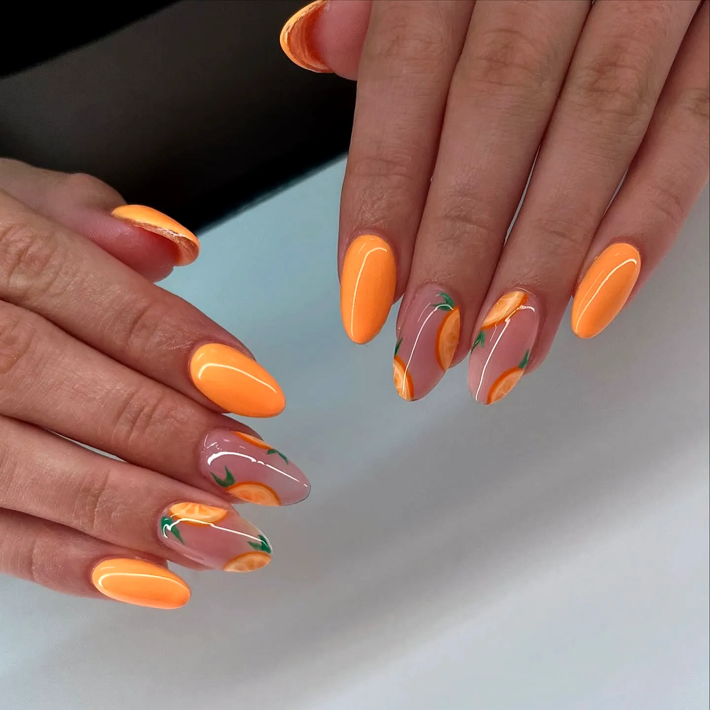 Cute almond-shaped orange nails with hand-painted fruit motifs and a stylish split design