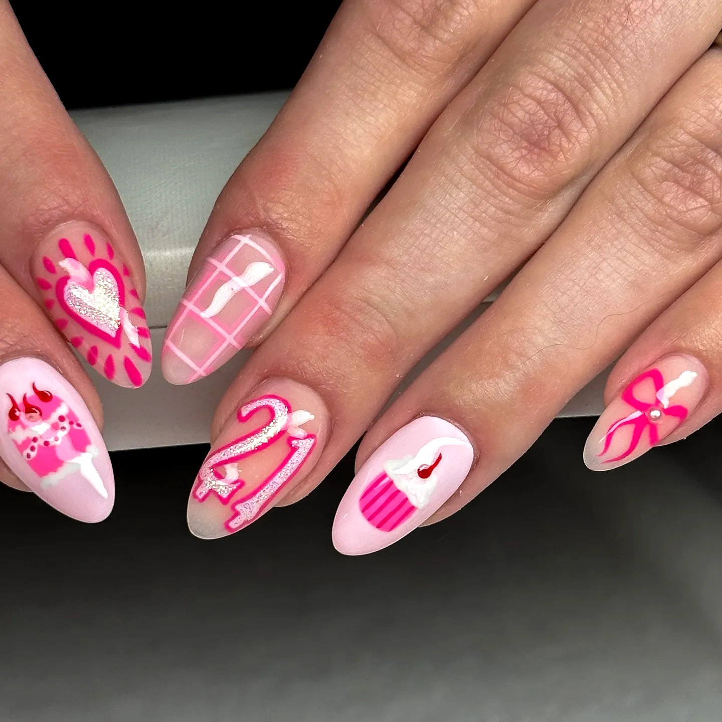 Cute almond-shaped pink birthday nails with playful cupcake and heart designs