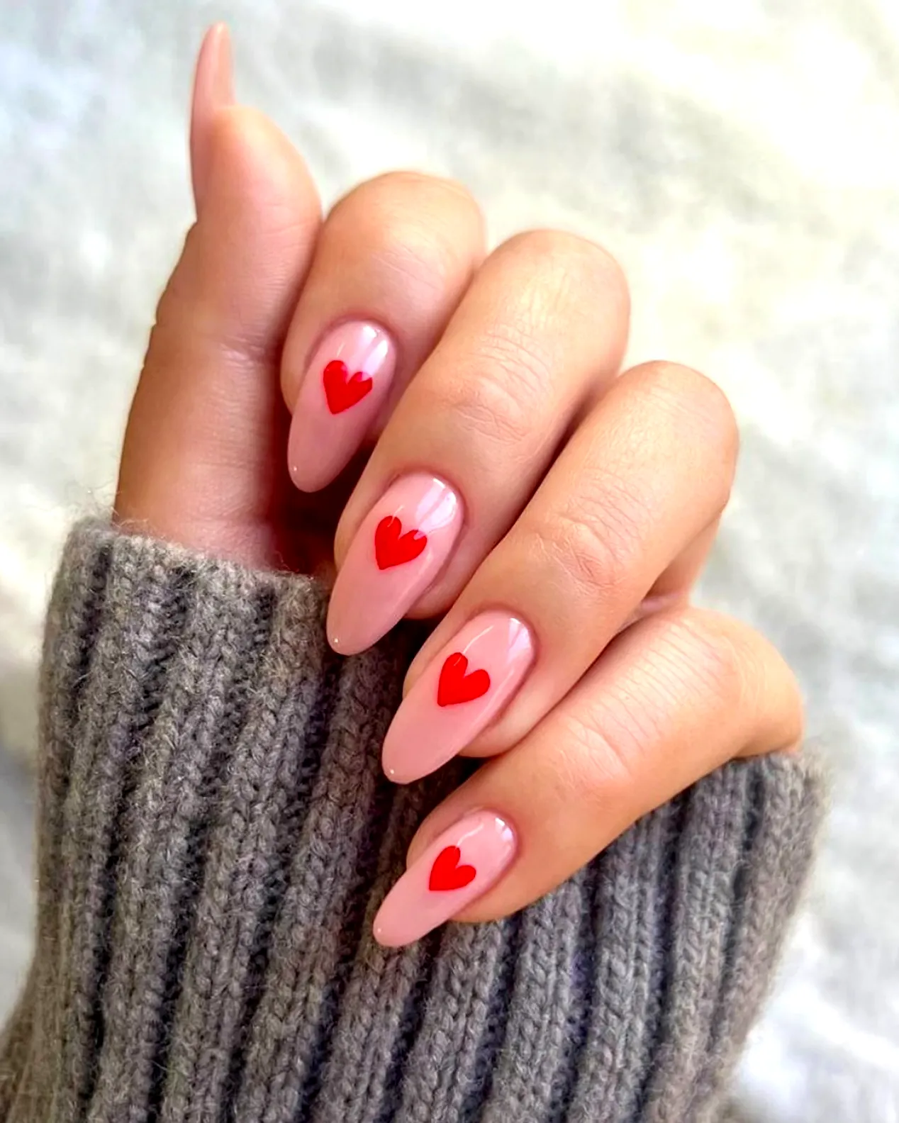 Cute almond shaped red heart nails with glossy pink base for a playful romantic look