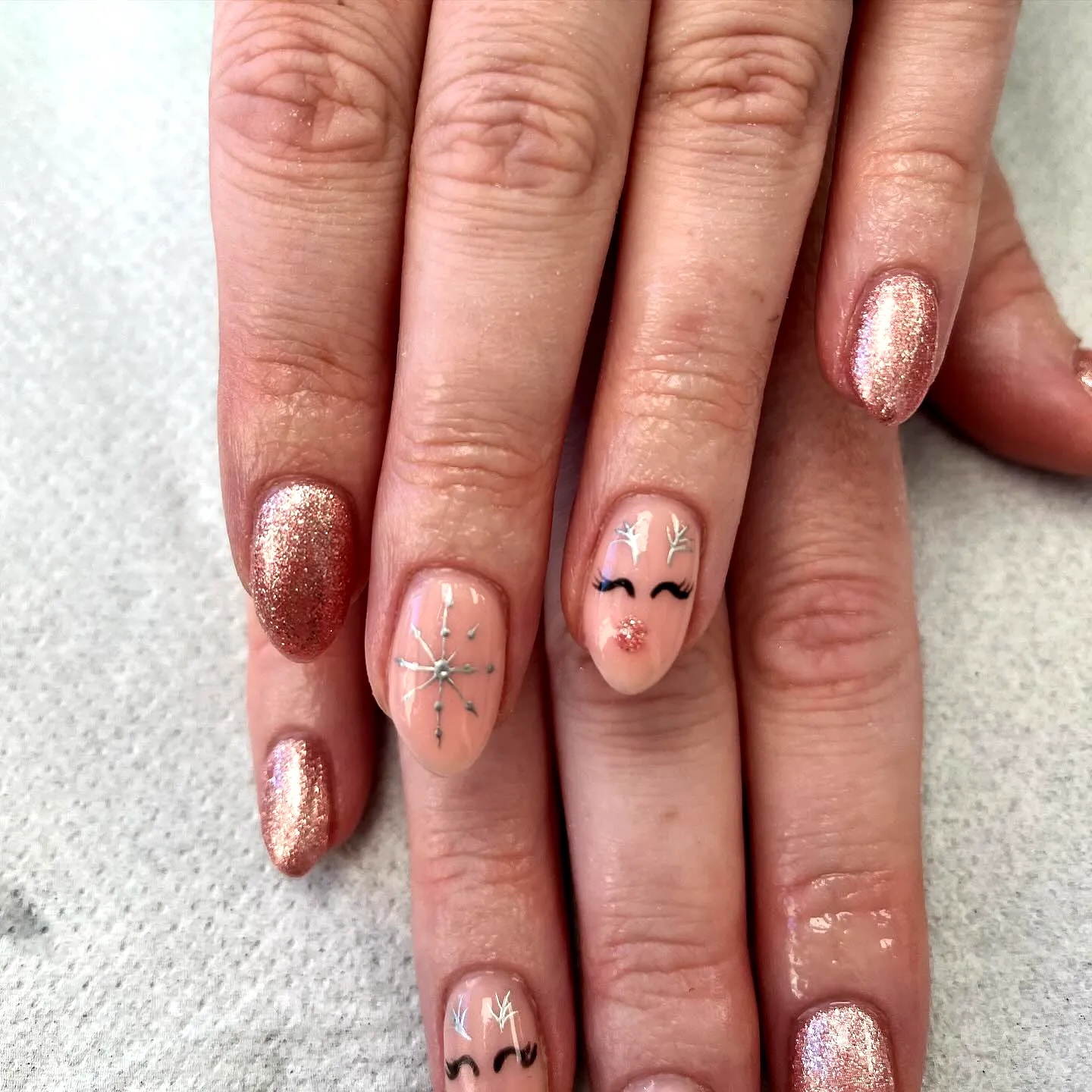 Cute almond-shaped reindeer nail designs in nude and rose gold with sparkling accents and hand-painted snowflakes