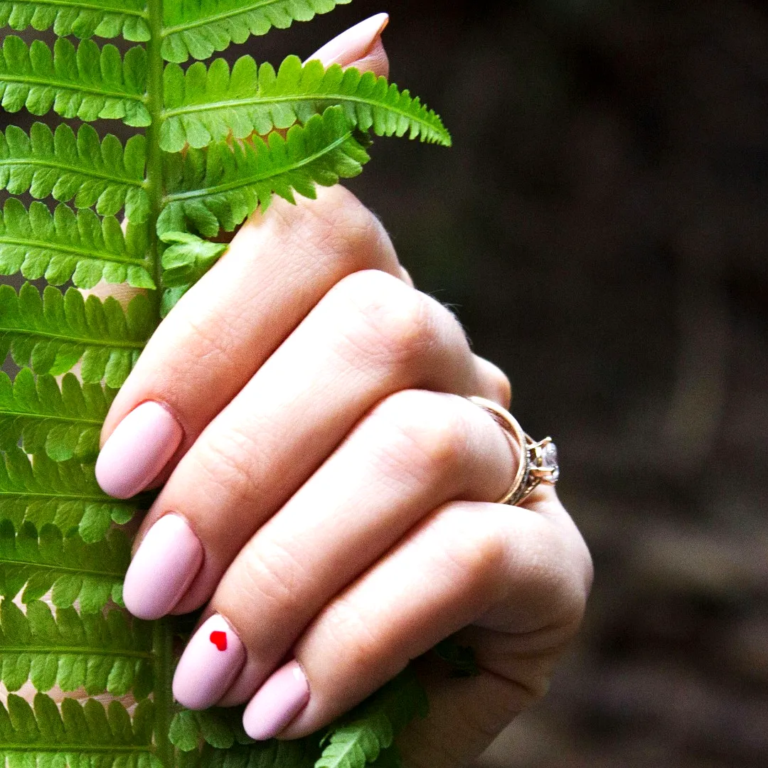 Cute oval shaped soft pink ring finger heart nails with glossy finish and romantic graphic design