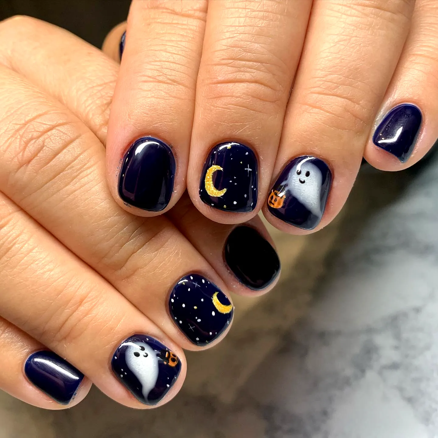Cute rounded ghost nail designs with navy and black shades featuring playful ghost illustrations crescent moons and star patterns