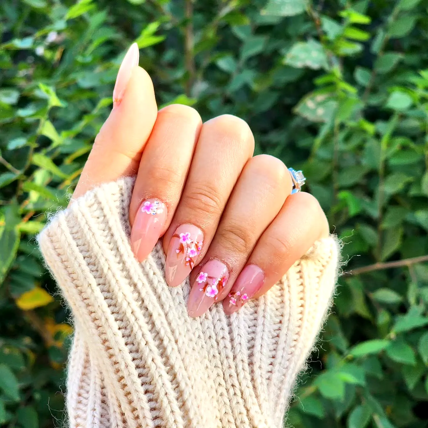 Elegant almond-shaped cherry blossom nails in soft beige with floral patterns and sparkly accents