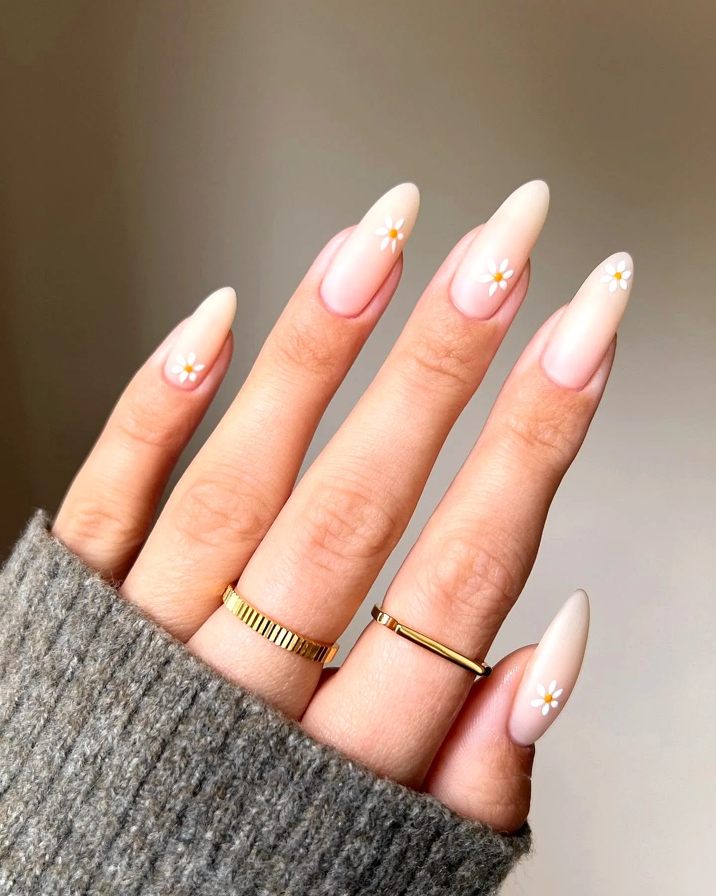 Elegant almond-shaped daisy nail designs with soft nude gradient and floral accents