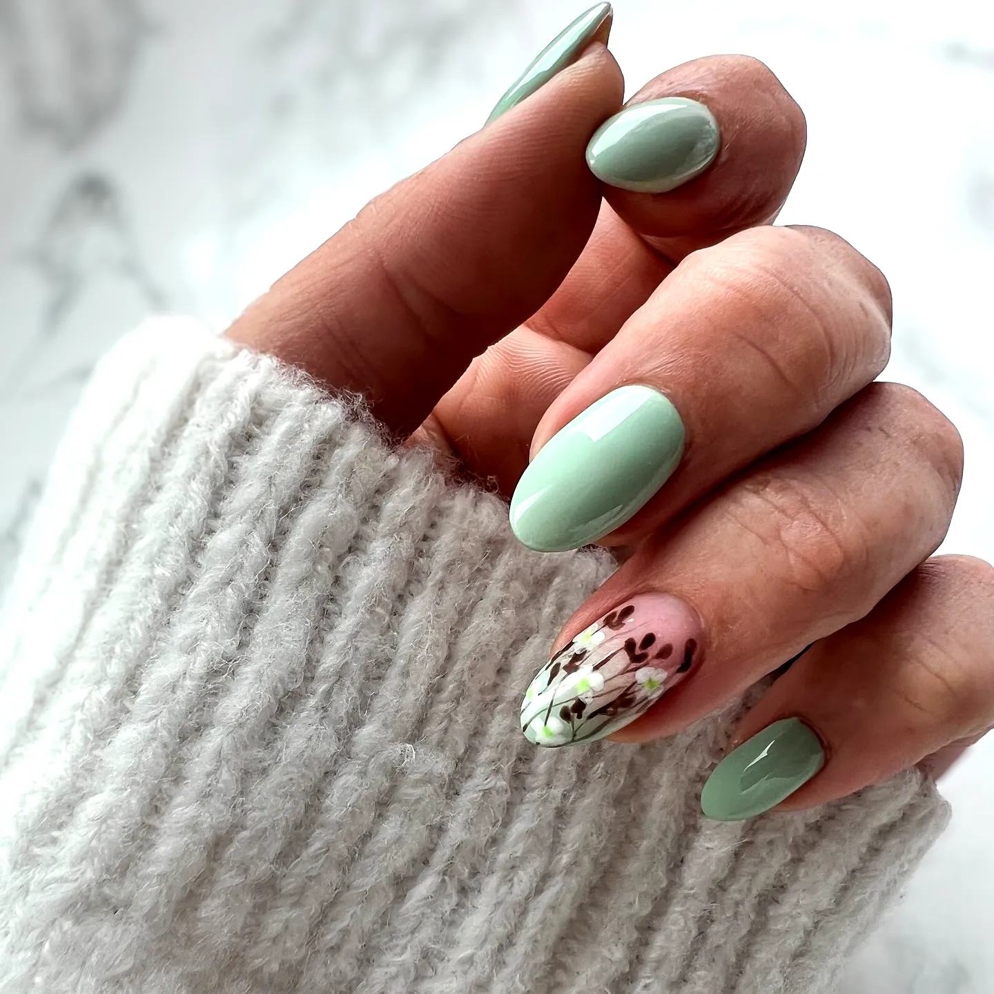 Elegant almond-shaped mint green nails with floral accent art for a modern look