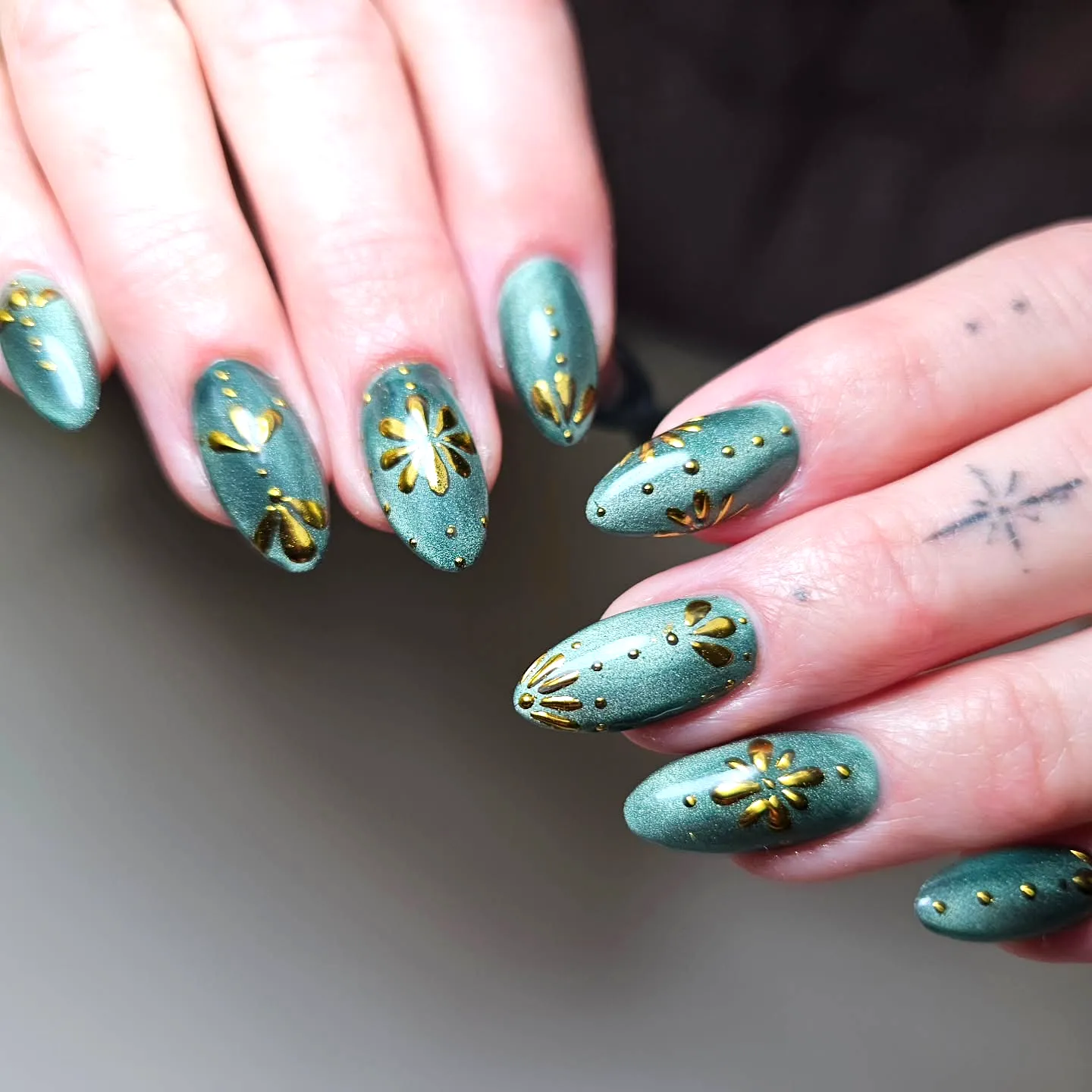Elegant almond-shaped muted green gold chrome nails with floral metallic art