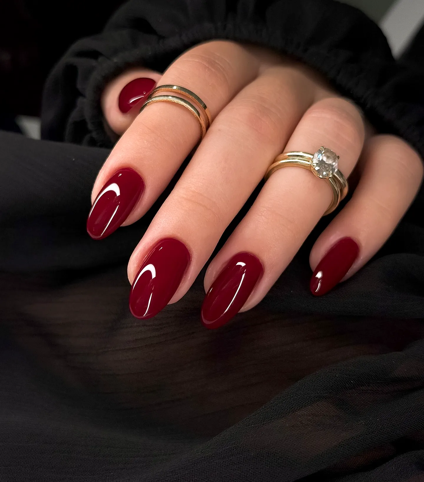 Elegant almond-shaped red nails featuring glossy burgundy polish with subtle white tips and chic gold accents