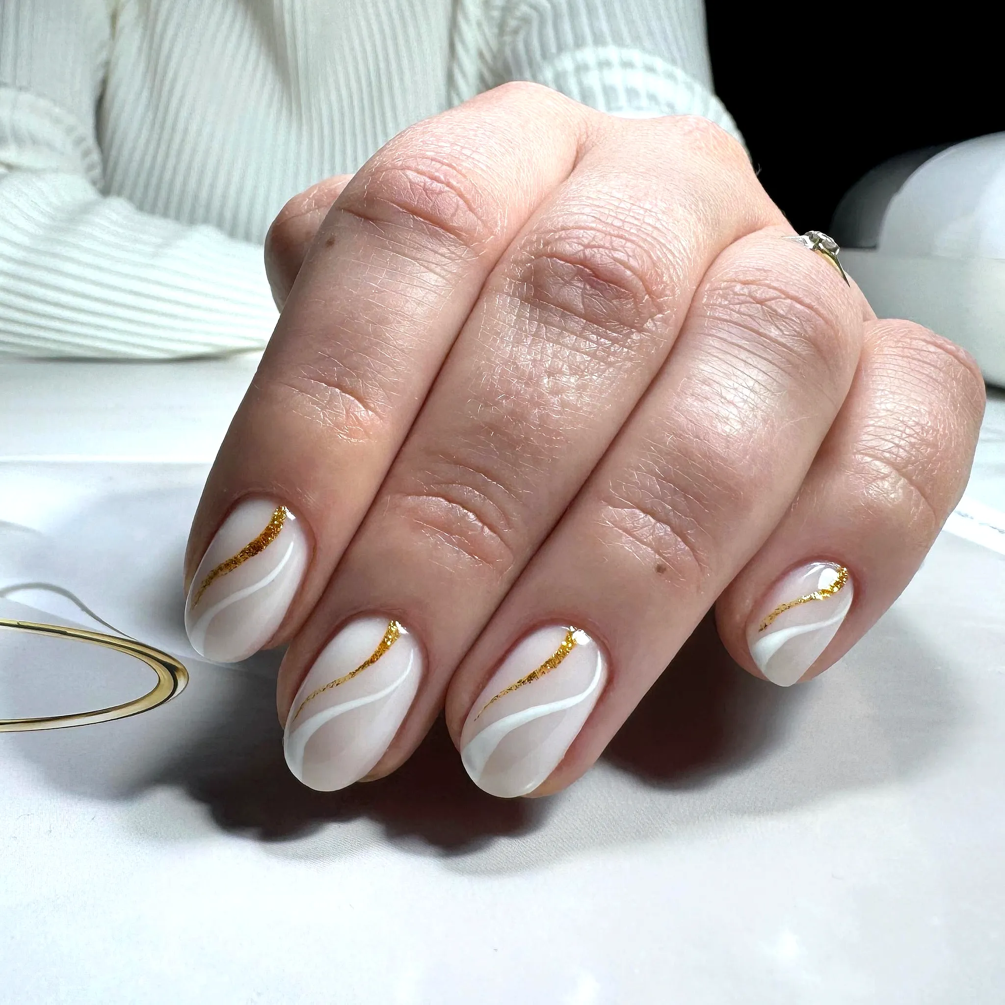 Elegant almond swirl nail designs in white with gold lines and glitter accents