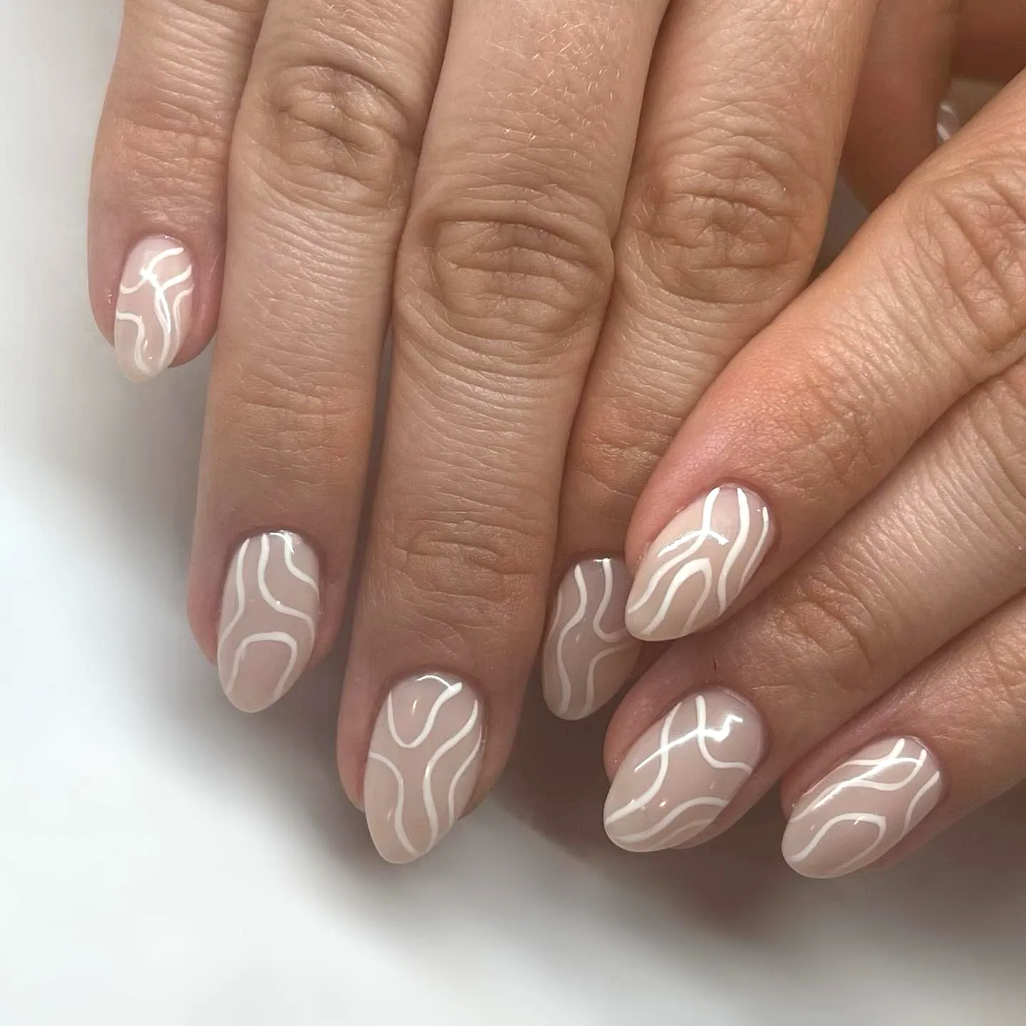 Elegant almond swirl nail designs with soft nude base and abstract white lines