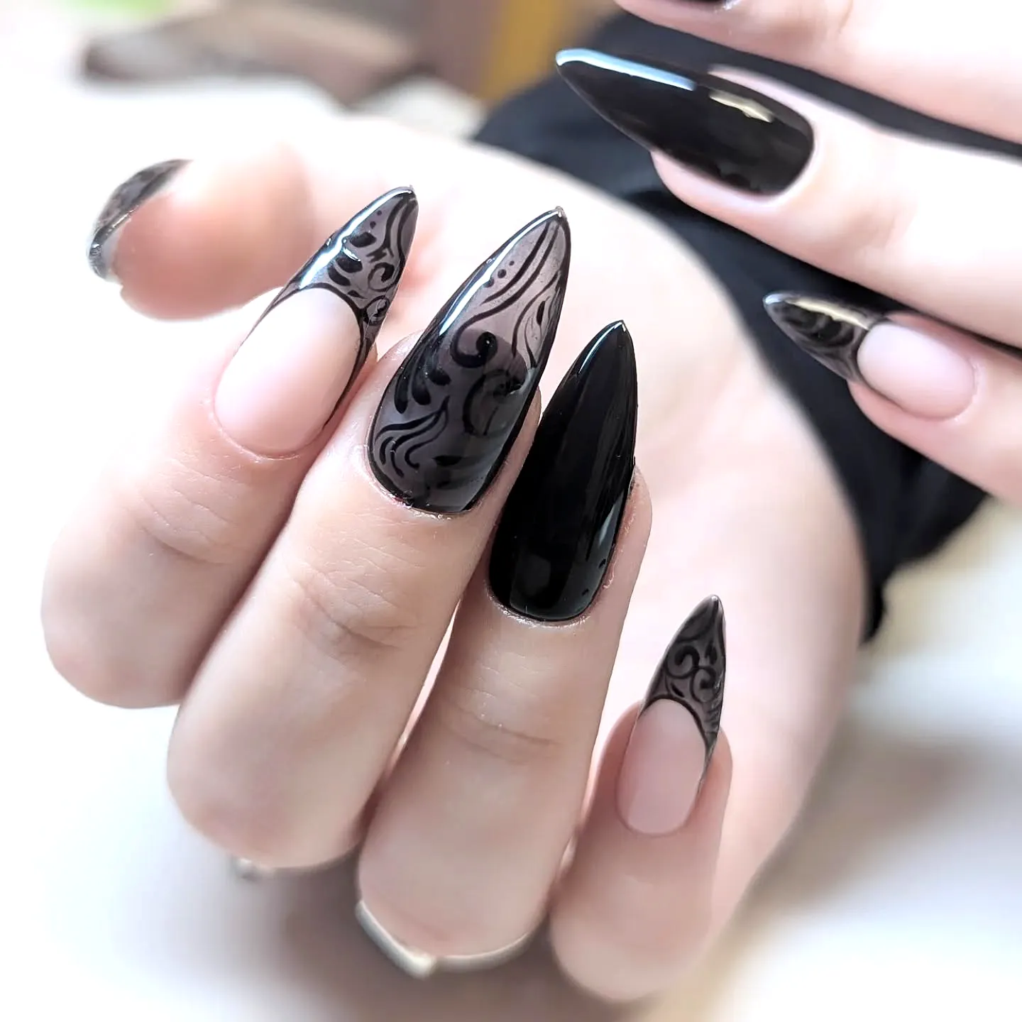 Elegant stiletto dark wedding nails with glossy black and nude polish featuring intricate swirl patterns