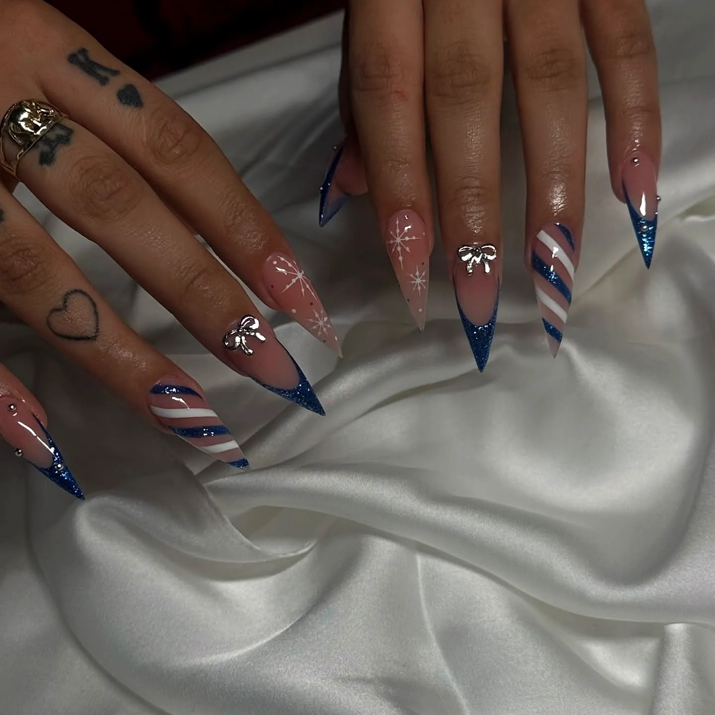 Elegant stiletto nails with nude and blue hues featuring silver accents and festive nail art designs