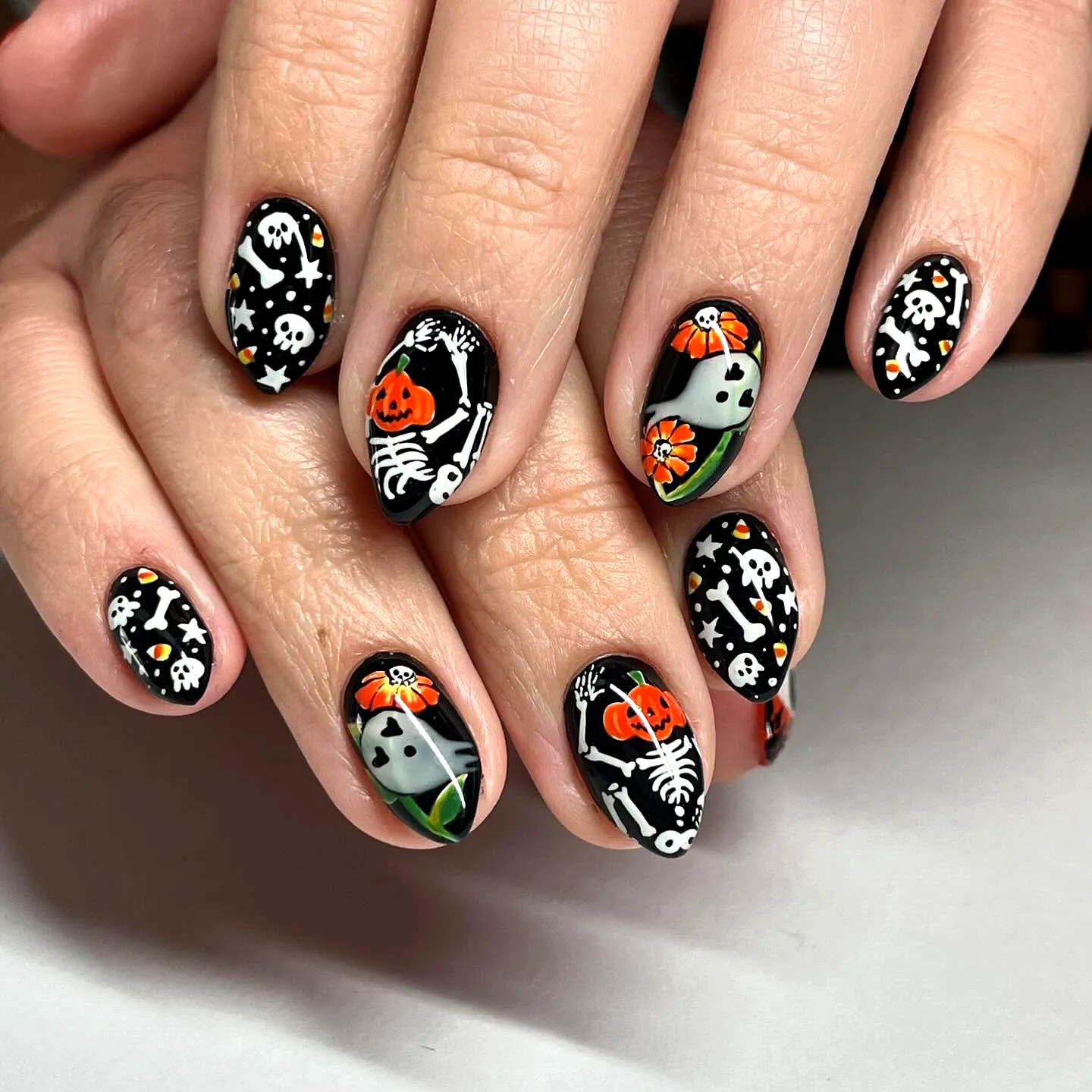 Spooktacular Almond Halloween Nails with Glossy Black Background and Colorful Pumpkin and Skeleton Nail Art