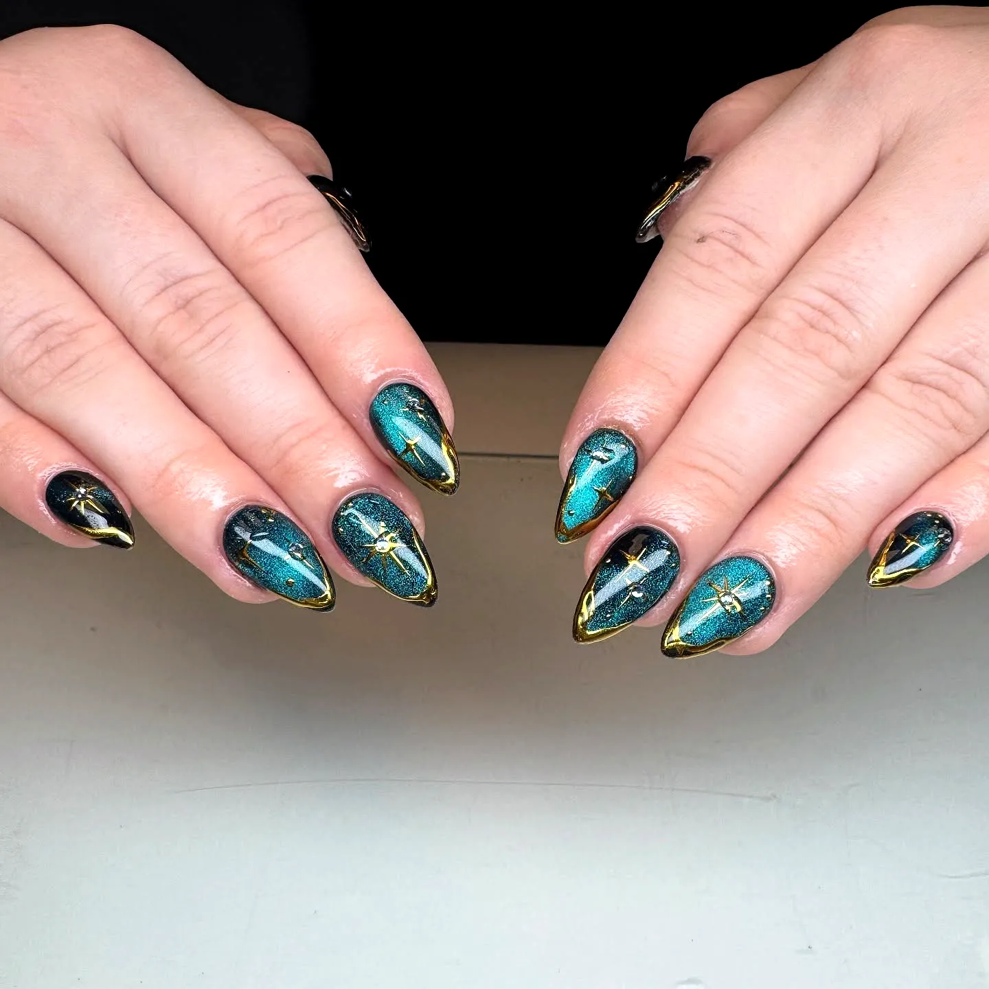 Stunning stiletto gold chrome nails with teal glossy finish and starry design