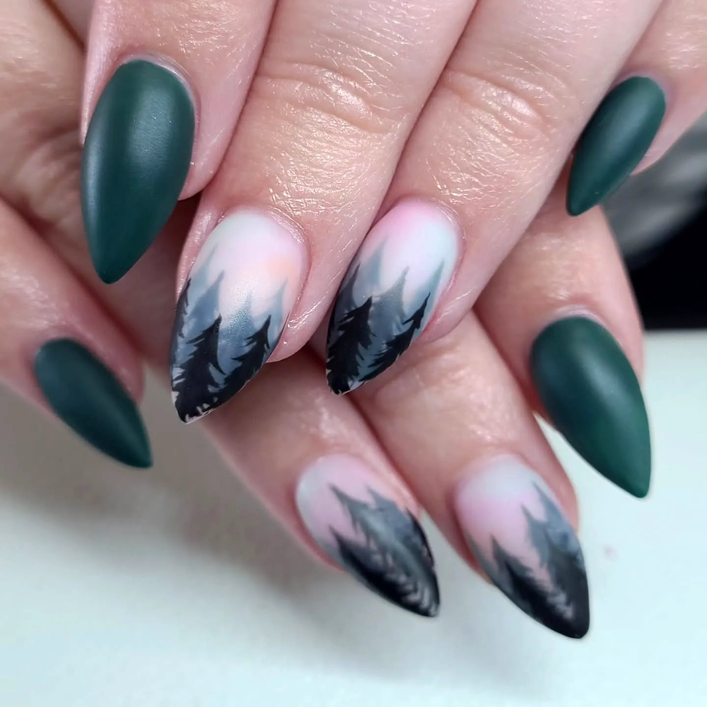 Stunning Stiletto Mountain Nails with Dark Green and Soft Pink Gradient and Intricate Black Silhouette Trees