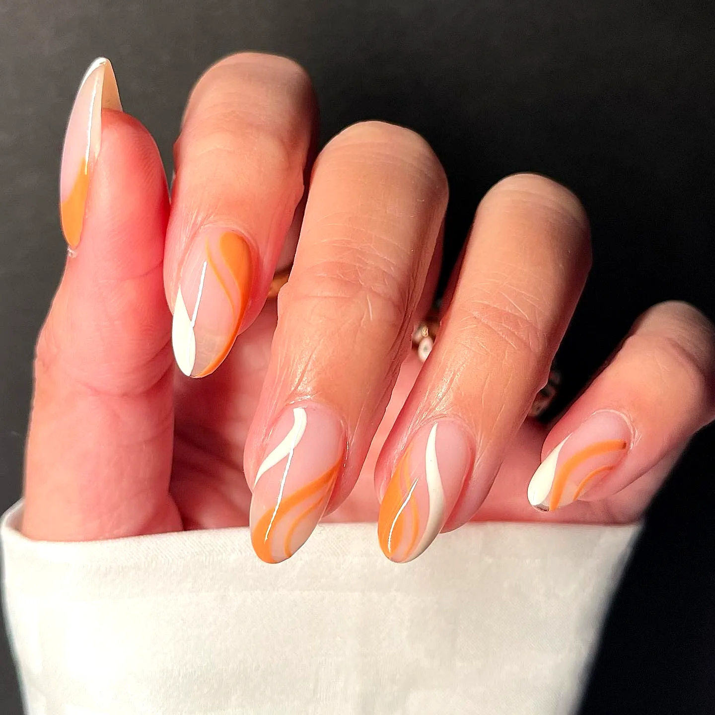 Stylish stiletto color block nails with bold orange and white swirls in a modern ombre design